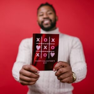 A joyful man presenting a Valentine's Day card with a red background, symbolizing love and celebration.
